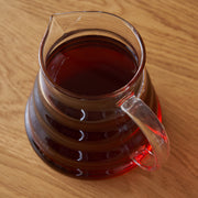 Glass pitcher filled with dark liquid on a wooden surface