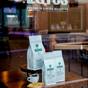 Caves coffee bags on a wooden table with a blurred cafe interior in the background