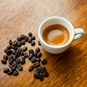 White cup of espresso with coffee beans on a wooden surface