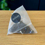 Tea bag with 'August' label on a wooden surface