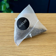 Tea bag with 'August' label on a wooden surface