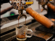 Espresso being poured from a machine into a glass measuring cup.