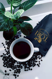 White cup of coffee with Tori Coffee Co. bag and scattered coffee beans on a marble surface with a plant.