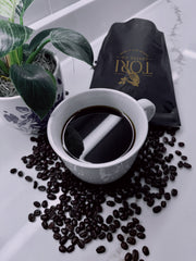 White mug with coffee, coffee beans, and a Tori coffee bag on a marble surface.