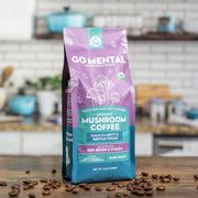 Go Mental Organic Mushroom Coffee package on a wooden surface with scattered coffee beans.