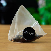Tea bag with 'AUGUST' label on a wooden surface