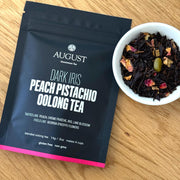 August tea package with a bowl of dark iris peach pistachio oolong tea on a wooden surface