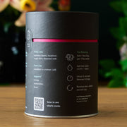 Black cylindrical container with pink band on a wooden surface, blurred flowers in the background