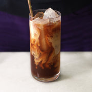 Glass of iced coffee with a straw on a white surface and dark background