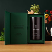 Green gift box with a black container labeled 'Rare Leaves' on a wooden surface.