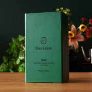 Green tea box labeled 'Rare Leaves Gold' on a wooden surface with a blurred floral background