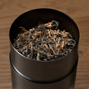 Black container filled with dried tea leaves on a wooden surface