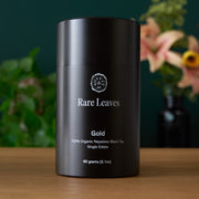 Black tea canister labeled 'Rare Leaves Gold' on a wooden surface with a blurred floral background