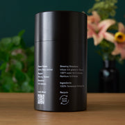 Black cylindrical container with text on a wooden surface with a blurred floral background