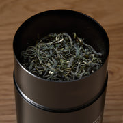 Black cylindrical container with dried green herbs on a wooden surface