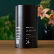 Black cylindrical container with text on a wooden surface with a blurred floral background