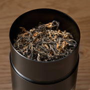 Black container filled with dried tea leaves on a wooden surface
