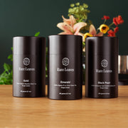 Three 'Rare Leaves' tea canisters on a wooden surface with a blurred floral background.