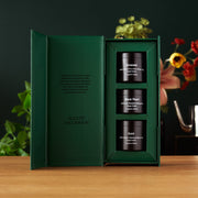 Green gift box with three black containers labeled 'Black Pearl', 'Gold', and 'August Uncommon' on a wooden surface.