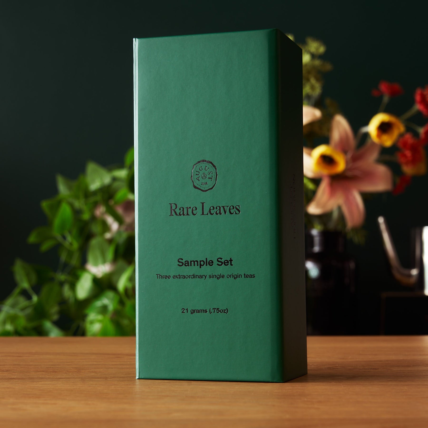 Green box labeled 'Rare Leaves Sample Set' on a wooden surface with a blurred floral background